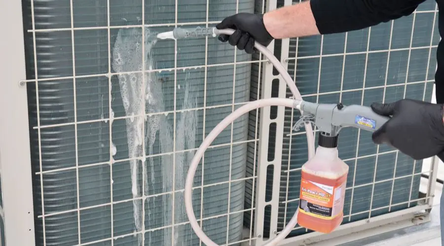 Person cleaning an air conditioning unit with soapy spray; maintaining HVAC equipment for optimal performance.