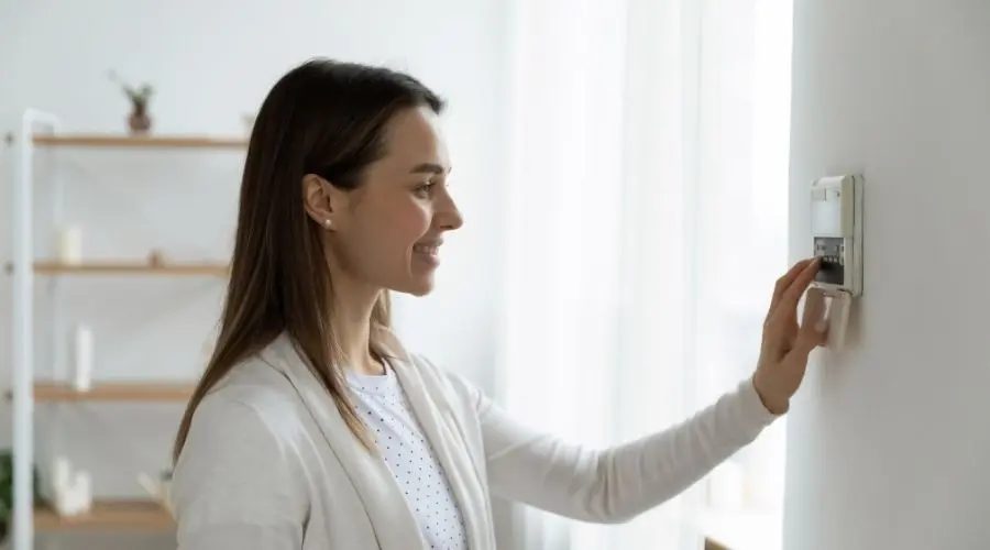 Woman adjusting a wall thermostat in a cozy, minimalist home, showcasing HVAC comfort and air conditioning maintenance.