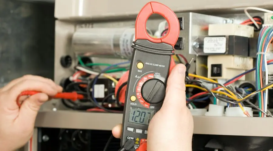 A technician using a clamp meter to test the voltage on an HVAC (Heating, Ventilation, and Air Conditioning) system.