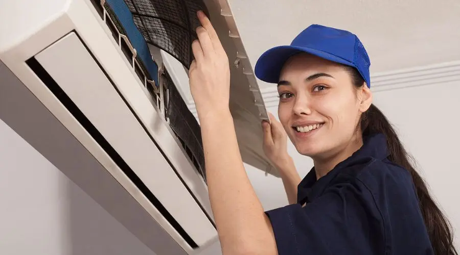 Female technician in a blue uniform servicing an air conditioning unit with tools at Boutwell's Air Masters.