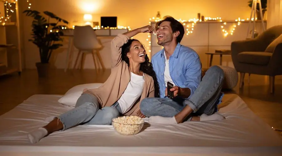 Couple enjoying movie night on a bed with popcorn and remote, in cozy indoor setting from Boutwell's Air Masters.