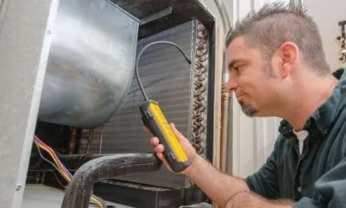 Male technician inspecting an HVAC refrigeration unit with testing device in industrial setting.