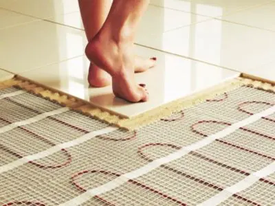 Feet standing on tile flooring above in-floor radiant heating system, demonstrating compatibility with various flooring types for enhanced warmth and comfort.