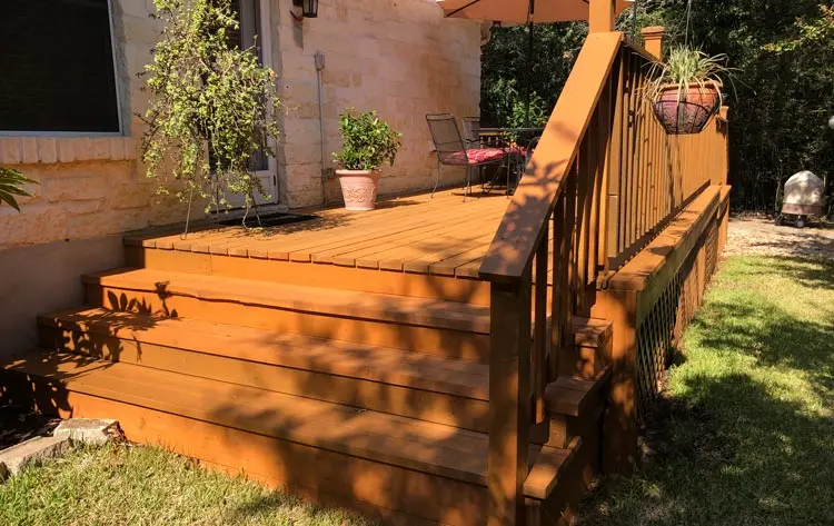 Deck installation featuring wooden steps and railing, surrounded by greenery, showcasing a well-maintained outdoor living space for home improvement in Austin.