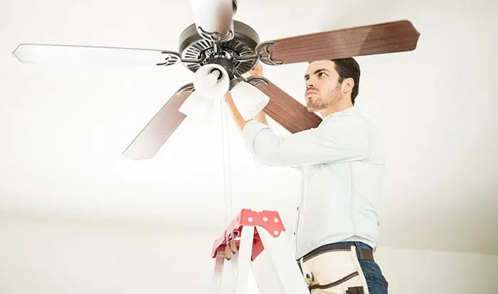 Man adjusting ceiling fan while standing on a ladder, illustrating handyman services for home electrical work and maintenance.