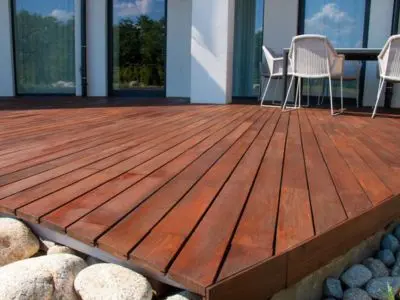 Decking materials showcasing a polished wooden deck with a modern design, surrounded by stones, emphasizing outdoor space customization and durability for home improvement.