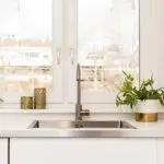 Modern kitchen sink with faucet, potted plants, and candle holders, illuminated by natural light.