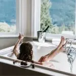 Person relaxing in a luxurious bathtub with mountain views and a champagne bucket—A-Plus service visuals.
