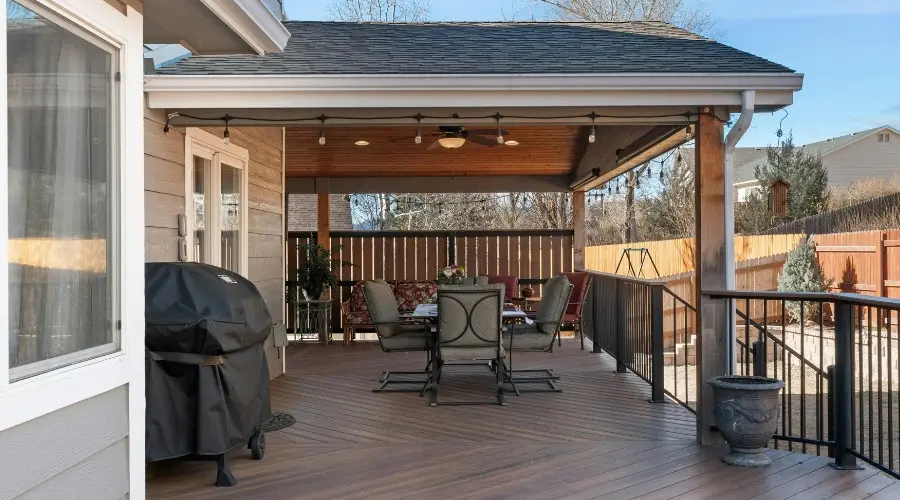 Covered patio with seating area, grill, and decorative plants, illustrating outdoor living space enhancements for winter enjoyment.