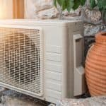 Air conditioning unit by stone walls and clay pot outdoors from A-Plus Air Conditioning & Home Solutions.