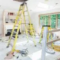 Yellow ladder in a construction area with debris, tools, and renovation materials, showcasing A-Plus home improvement work.