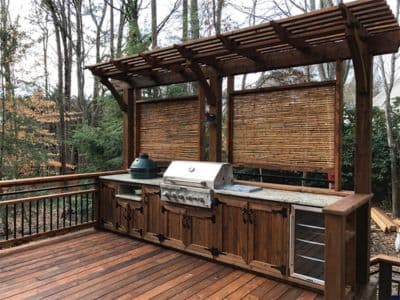 Outdoor kitchen with a grill and countertop under a wooden pergola on a deck, surrounded by trees, ideal for enhancing outdoor entertaining spaces.