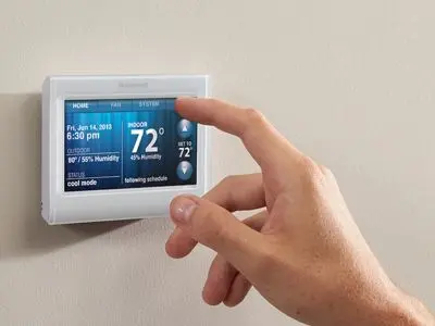 Hand adjusting a programmable thermostat displaying indoor temperature of 72°F, highlighting control over in-floor radiant heating systems for enhanced home comfort and energy efficiency.