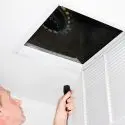Person inspecting a duct with a flashlight for A-Plus Air Conditioning maintenance services, emphasizing home accessibility.
