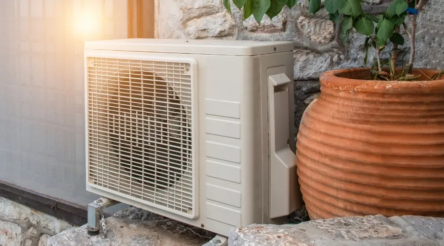 Heat pump unit installed outside a home, surrounded by stone wall and potted plant, illustrating energy-efficient HVAC solutions for heating and cooling.