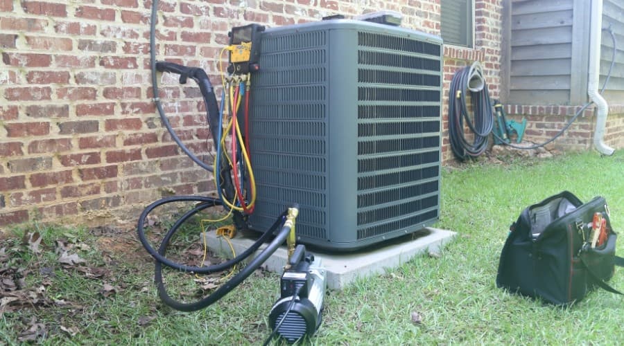 Air conditioning unit and repair tools against brick wall, indicative of AC repair services.