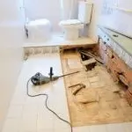 Partially renovated bathroom with two toilets and construction tools, showcasing ongoing work by A-Plus Home Solutions.