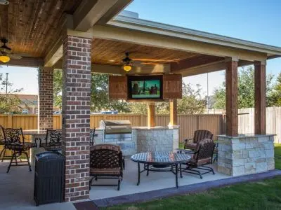 Patio with a roof, outdoor seating, grill, and mounted TV, showcasing a winter-friendly entertainment space.
