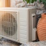 Heat pump unit installed beside decorative pot and stone wall, illustrating HVAC system for energy efficiency in residential settings.