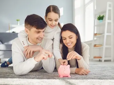 Family saving money together, placing coins in a pink piggy bank on a cozy living room floor, emphasizing financial planning and energy savings from heat pump installation.
