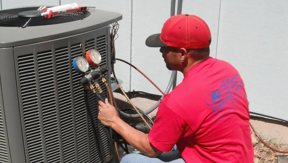 Technician in red shirt servicing air conditioning unit, highlighting A-Plus Air Conditioning & Home Solutions' repair services in Austin, TX.