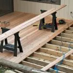 Wooden boards and sawhorses on a deck under construction for outdoor entertaining by A-Plus Solutions. Tools visible.