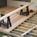 Wooden boards on saw horses for deck installation by A-Plus Home Solutions, showcasing tools and an unfinished structure.