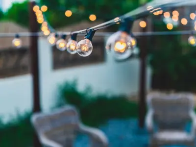 String lights illuminating a patio area with wicker chairs, enhancing outdoor ambiance and usability during evening gatherings.