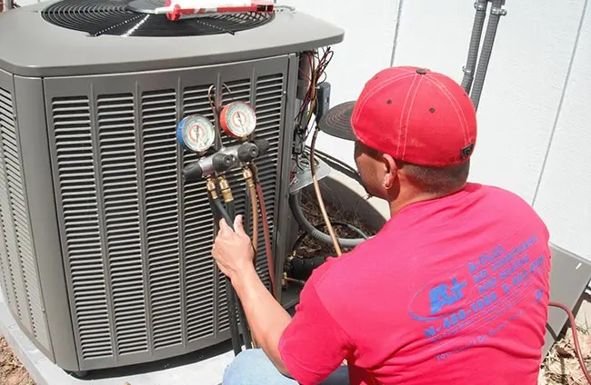 Technician servicing air conditioning unit with gauges, representing A-Plus Air Conditioning & Home Solutions' repair and maintenance services in Pflugerville, TX.
