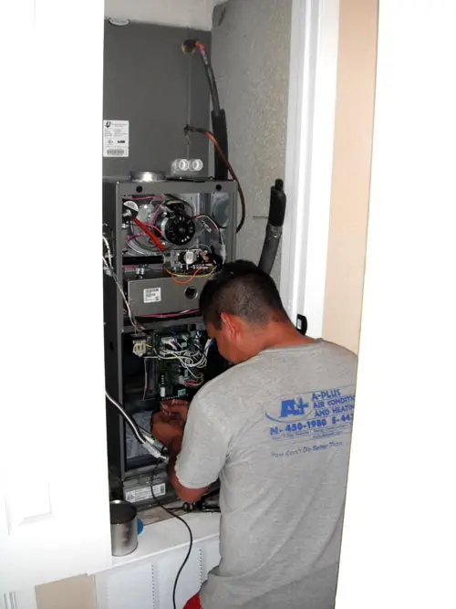 Technician repairing a gas furnace, showcasing A-Plus Air Conditioning & Home Solutions branding, in a residential setting.