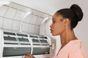 Woman inspecting an air conditioning unit, emphasizing the importance of regular maintenance and clean air ducts for improved indoor air quality.