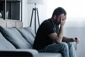 Man sitting on a couch with head in hand, expressing distress, highlighting the importance of comfortable living conditions supported by HVAC services.
