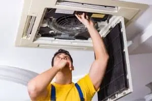 HVAC technician performing maintenance on ceiling air conditioning unit, focusing on repair and system efficiency for Atlantic Heating & Air Conditioning.