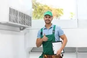 HVAC technician giving a thumbs-up next to an air handler, representing air handler services and maintenance for efficient home cooling.