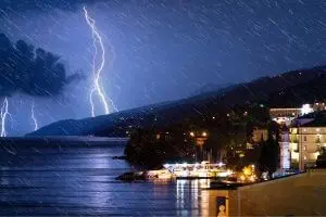 Stormy night with lightning illuminating the sky over a coastal town, showcasing the impact of climate change and the importance of community action for environmental stewardship.