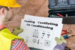 HVAC technician reviewing schematic diagram labeled "Heating Ventilating Air Conditioning" while preparing tools for maintenance or repair work.