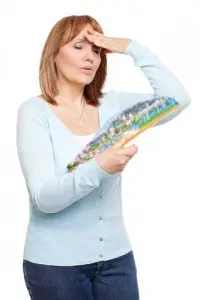 Woman fanning herself with a colorful fan, appearing overheated, illustrating discomfort from high temperatures related to air conditioning issues.