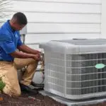 Technician in blue uniform servicing an air conditioning unit with tools for Atlantic Heating & Air Conditioning maintenance.