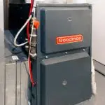Goodman furnace with gray exterior and red logo, showing pipes and wiring in a practical HVAC installation setting.
