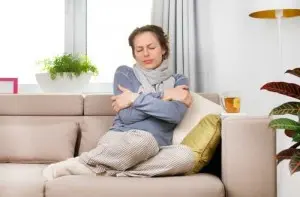 Woman sitting on a couch, wrapped in a scarf, appearing cold and uncomfortable, emphasizing the need for effective heating solutions in homes.