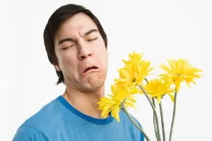 Man grimacing while holding yellow flowers, illustrating allergy discomfort related to seasonal changes and indoor air quality concerns.