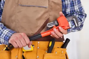 Person in work attire holding a pipe wrench, emphasizing HVAC maintenance tools for improving indoor air quality and system readiness for summer.