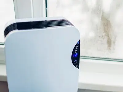 Dehumidifier appliance displaying humidity level next to a foggy window, illustrating air quality improvement for healthier indoor environments.