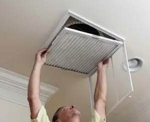 Person changing HVAC air filter in ceiling vent for improved indoor air quality and system efficiency.