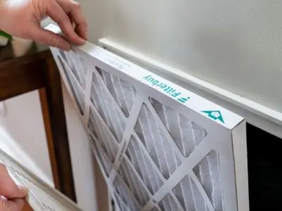 Hand replacing an air filter in an HVAC system, emphasizing indoor air quality maintenance and the importance of regular filter changes for healthier living environments.
