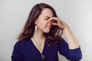 Woman grimacing while pinching her nose, indicating a strong unpleasant smell, related to air quality concerns in HVAC systems.