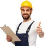 Male construction worker in safety gear smiling and holding clipboard, promoting professional HVAC repair services.