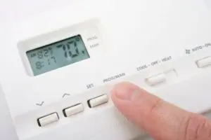 Digital thermostat displaying temperature settings with a finger adjusting the controls, relevant to HVAC checks for home insulation and heating efficiency.
