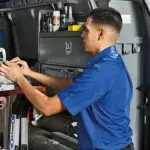 Service technician in blue uniform with HVAC tools inside a van, representing Atlantic Heating & Air Conditioning.