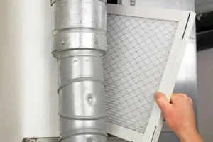Hand removing a dirty HVAC filter from a duct, emphasizing air quality management during home renovations.